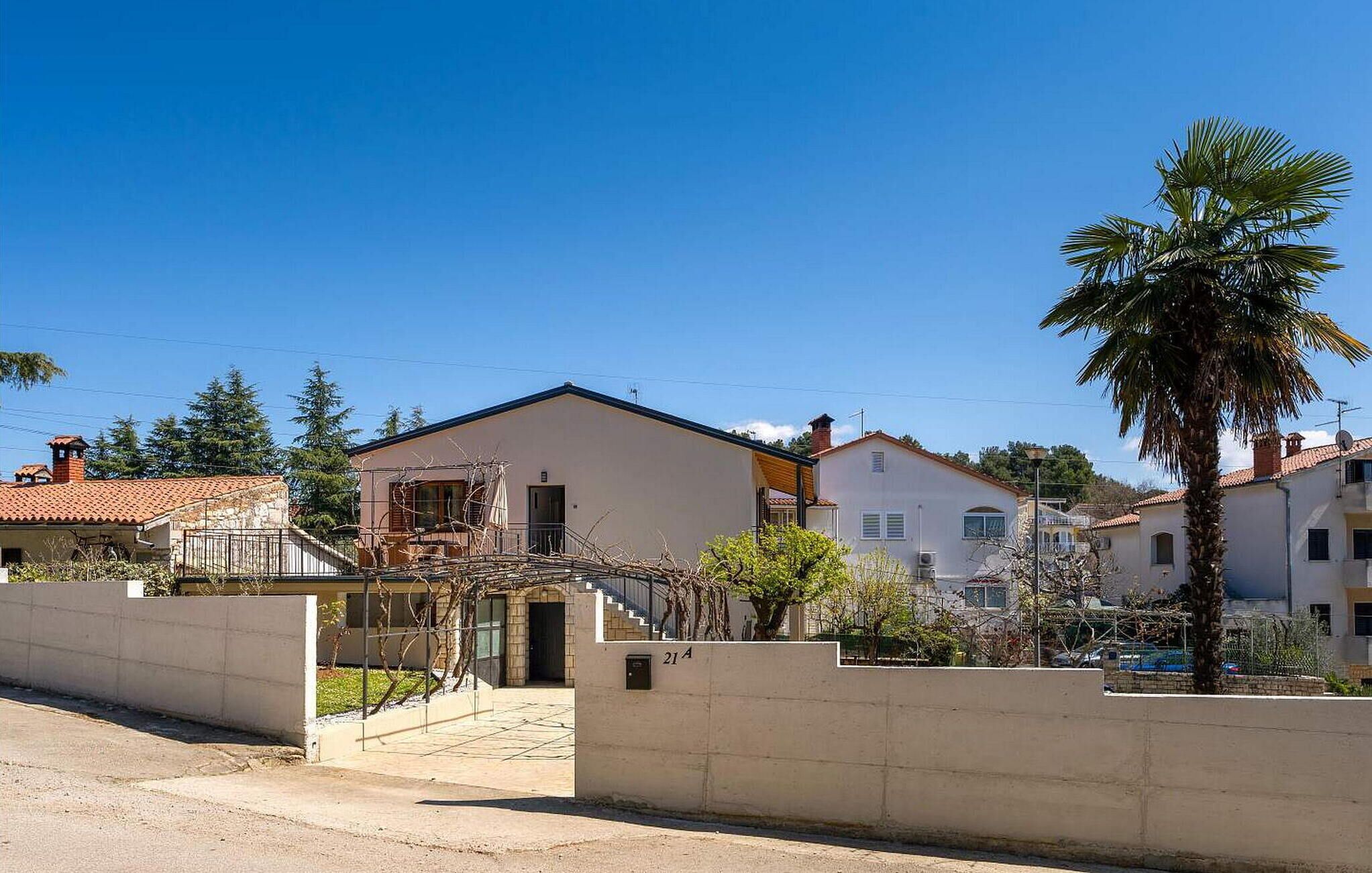 Un quartier résidentiel avec une maison blanche, un palmier et un ciel bleu dégagé.