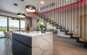 Contemporary living space with a central island, modern staircase, and seating area.