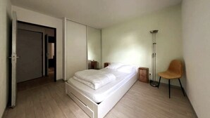 Un dormitorio con cama, una silla, una lámpara de pie y un armario.