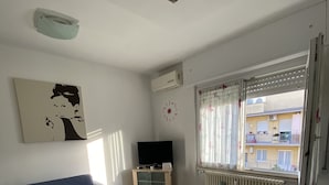 A living room with a blue sofa, a TV stand, a radiator, and a window with curtains.