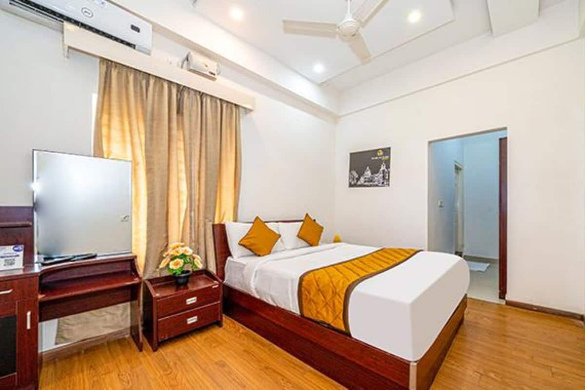 Quarto de hotel com cama, escrivaninha, televisão e janela com cortinas.