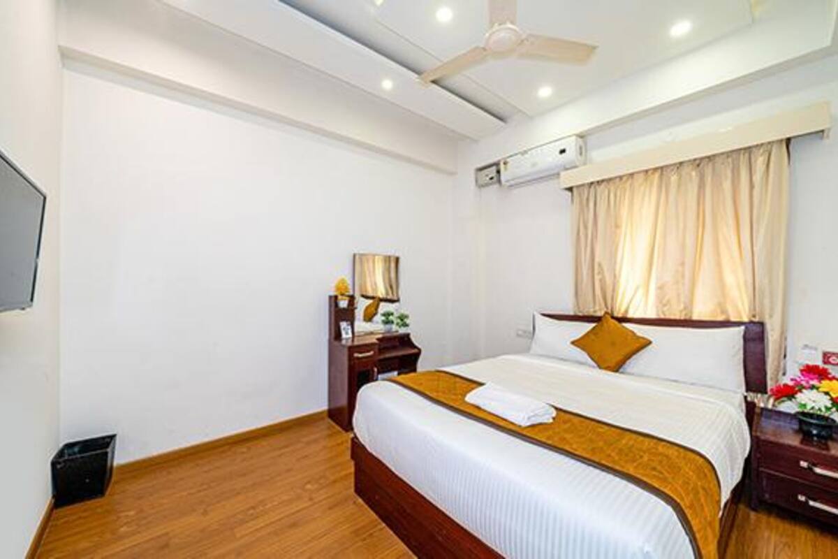 Quarto de hotel com cama, mesa de cabeceira, televisão e ventoinha no teto.