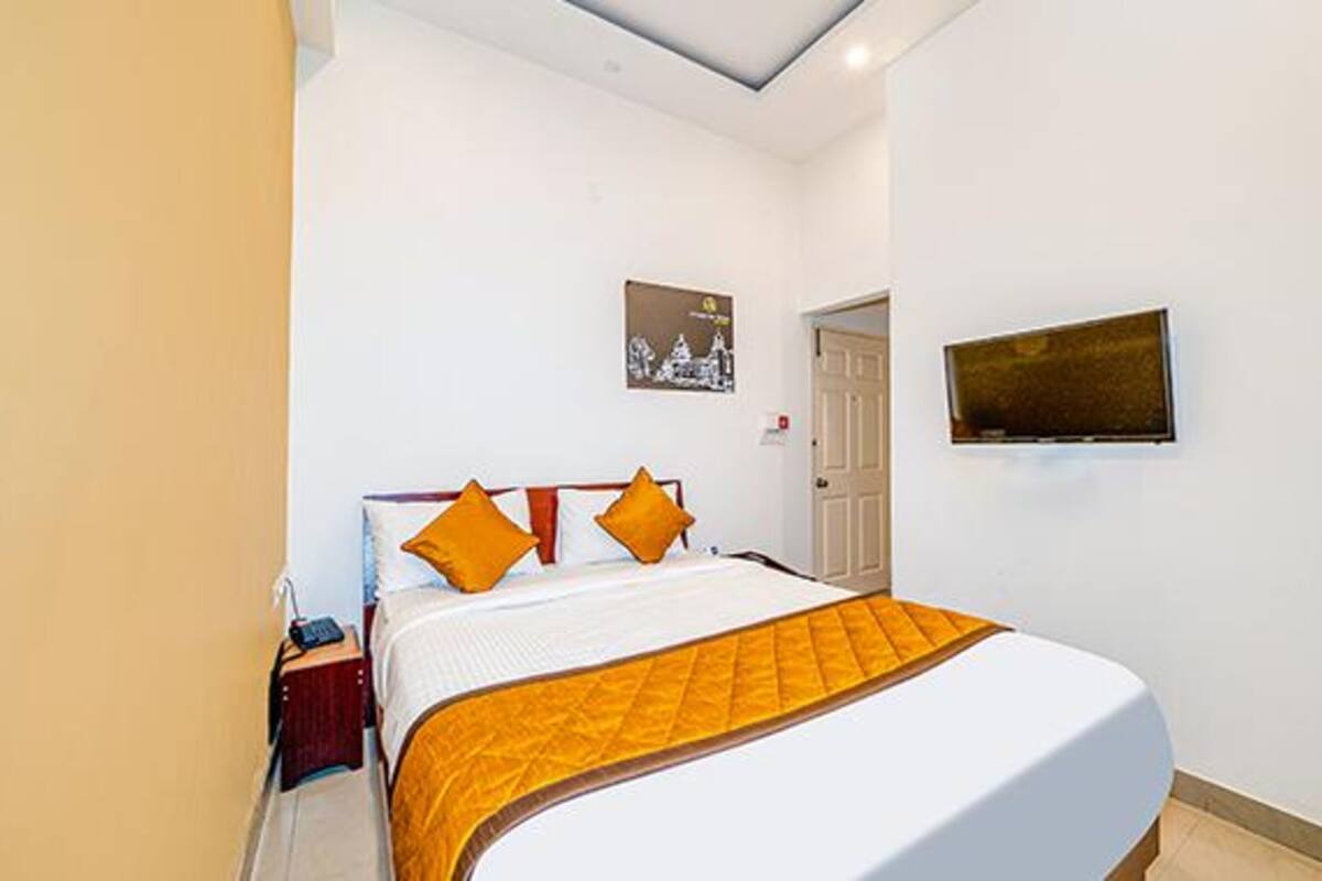 Quarto de hotel com cama, mesa de cabeceira, TV na parede e uma porta.