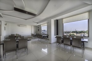 A modern dining area with a city view, large windows, and contemporary furniture. - Fabhotel Signature Inn (Jaipur)