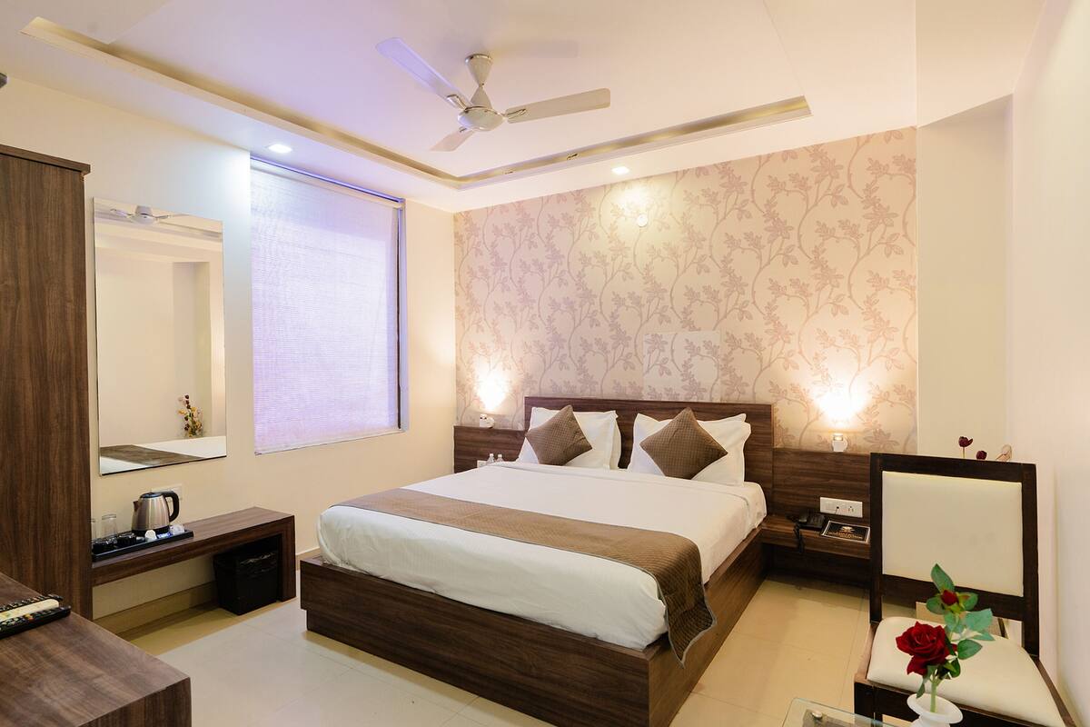 A hotel room with a large bed, bedside tables, a nightstand, a mirror, a ceiling fan, and a floral wallpaper.