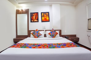 Habitación de hotel con una cama grande, dos cuadros en la pared y una mesita de noche de madera con un teléfono.