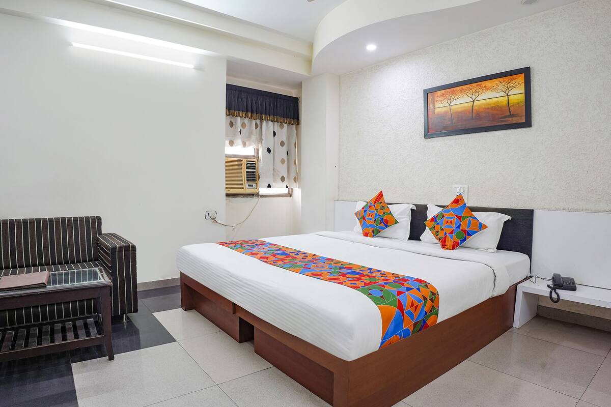 A hotel room with a bed, a sofa, a bedside table, a phone, and a window with curtains.