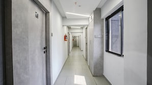 A long, narrow hallway with doors on both sides, a fire extinguisher mounted on the wall, and a window on the right side. - Fabhotel Aahan (Navi Mumbai)