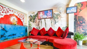 A modern lobby with a red sofa, a glass coffee table, a fish tank, and a mural on the wall. - Fabhotel Prithviraj (Indore)