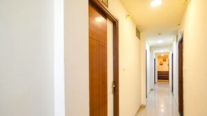 A corridor with wooden doors and white walls. - Fabhotel Prithviraj (Indore)