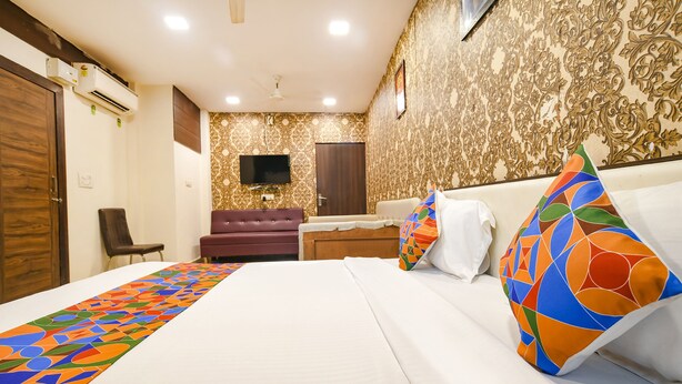 A hotel room with a large bed, a TV mounted on the wall, a sofa, and a patterned wallpaper. - Fabhotel Prithviraj (Indore)