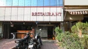 A restaurant with a signboard, a motorcycle parked in front, and a potted plant nearby. - Fabhotel Prithviraj (Indore)