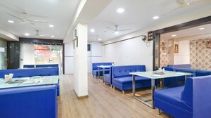 A restaurant with blue booths and tables, ceiling fans, and recessed lighting. - Fabhotel Prithviraj (Indore)