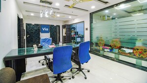 A modern office space with a glass partition, a ceiling fan, and a desk with chairs. - Fabhotel Apple Tree (Guwahati)