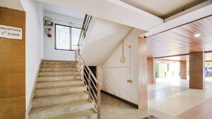A staircase leading to the 1st floor reception area, with a fire extinguisher mounted on the wall and a window above. - Fabhotel Apple Tree (Guwahati)