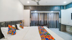 A hotel room with a bed, a ceiling fan, a desk, and a view of the outside through curtains. - Fabhotel Apple Tree (Guwahati)