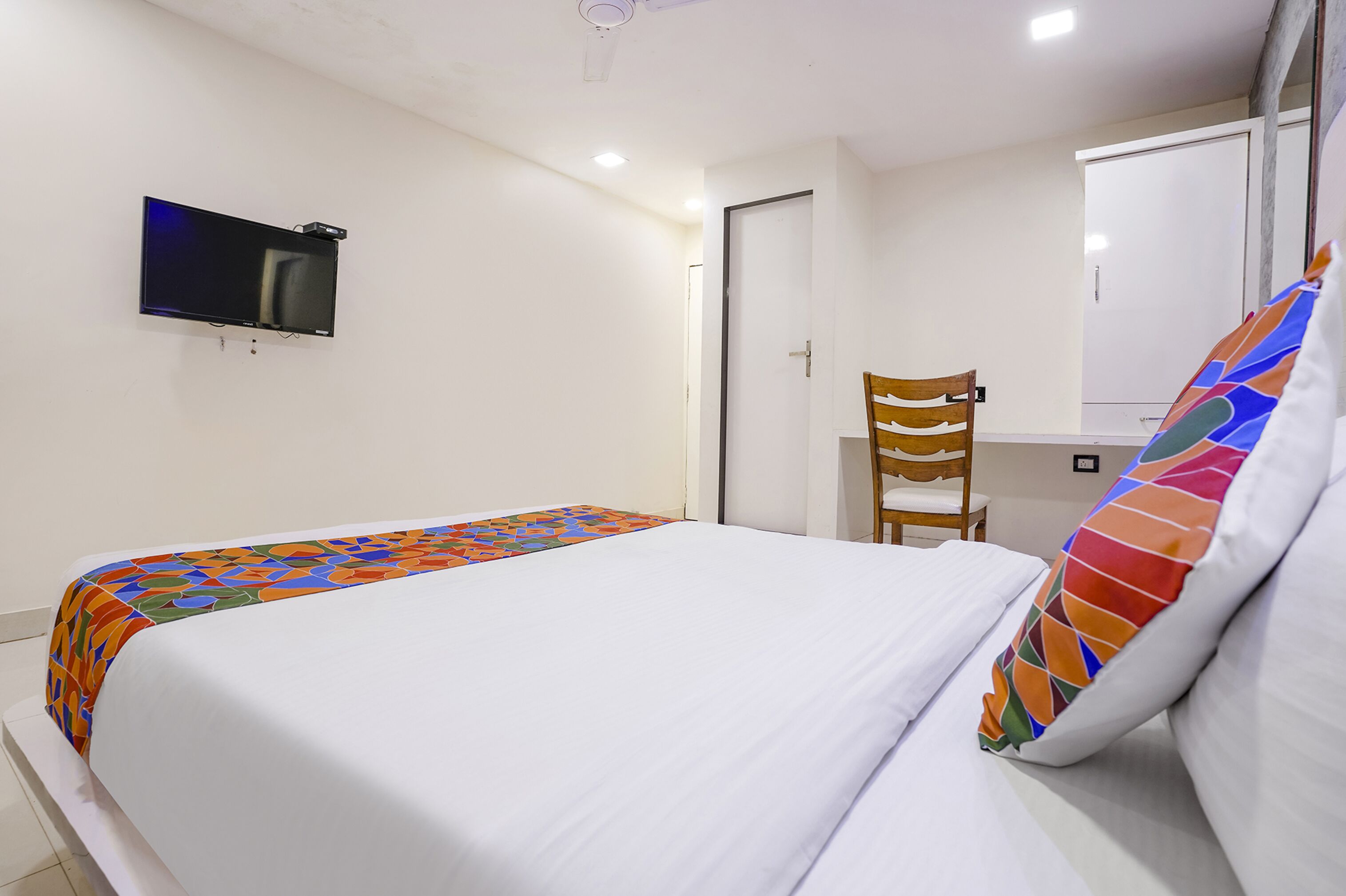 A hotel room with a bed, a television mounted on the wall, a chair, and a window.