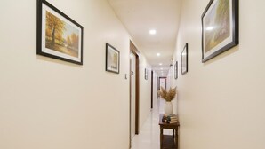 A hallway with framed pictures on the walls, a wooden table with a vase and books, and a tiled floor. - FabHotel Golden Star (Mumbai)