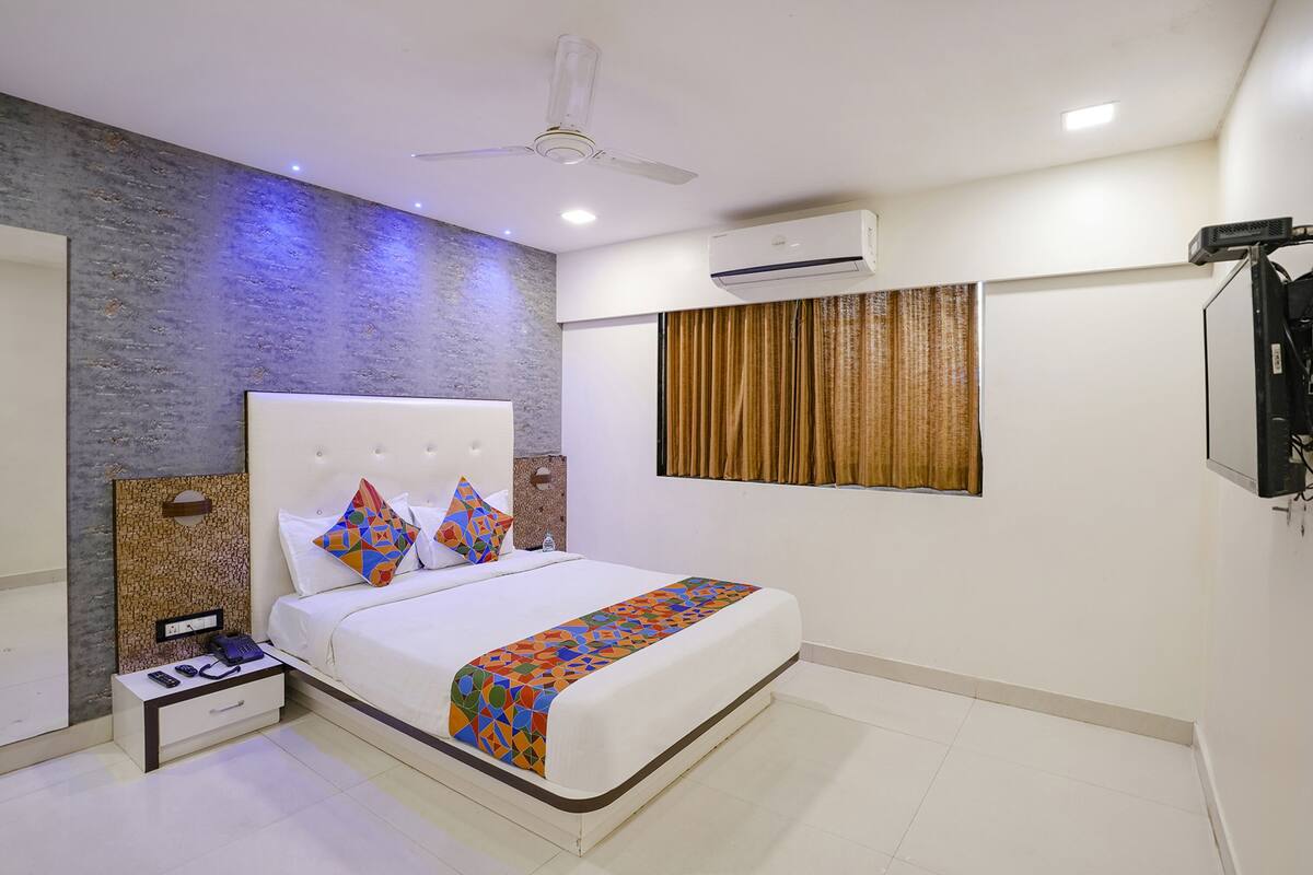 A modern bedroom with a white bed, a nightstand with a phone and glasses, a ceiling fan, and an air conditioning unit.