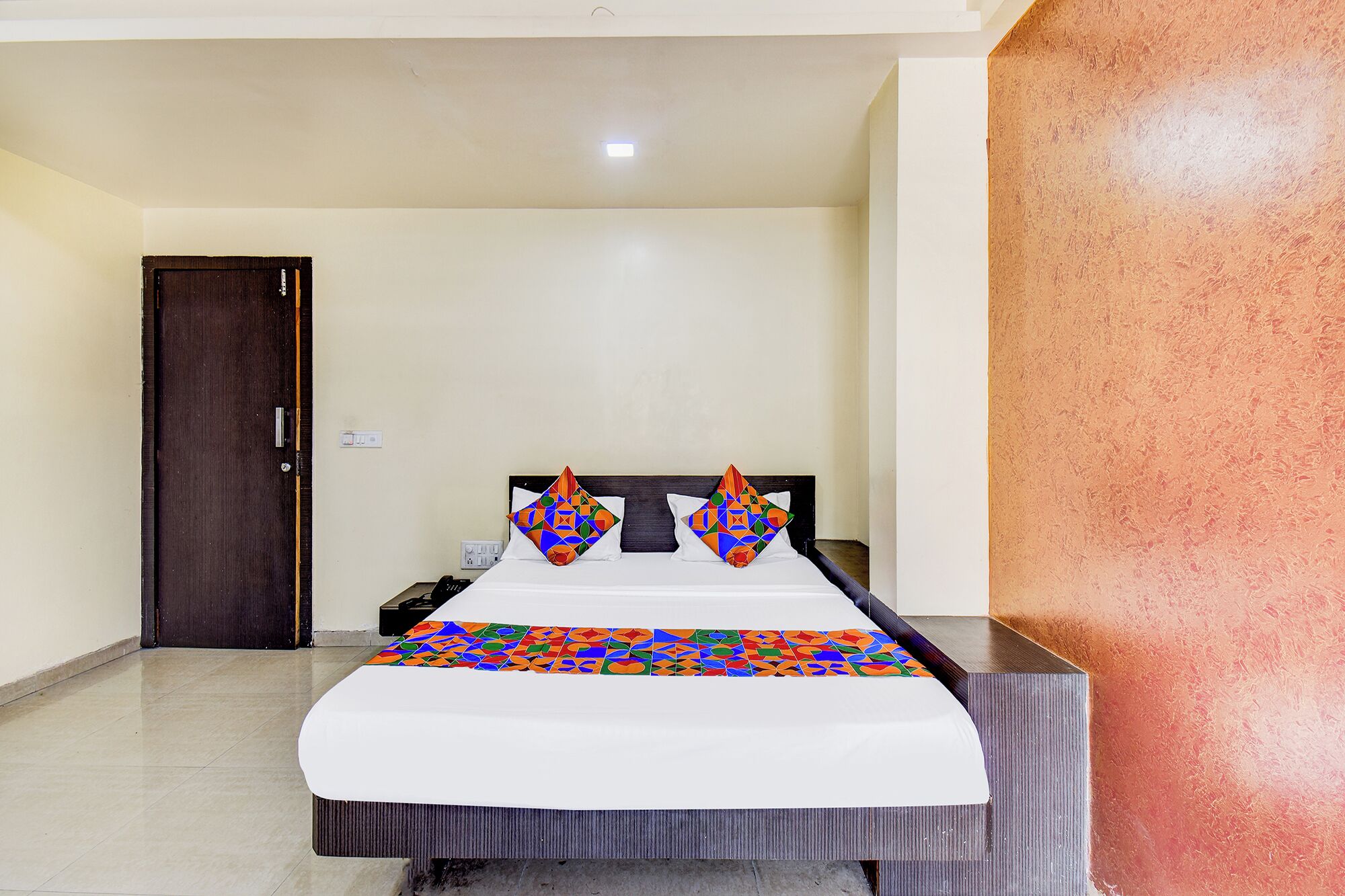A hotel room with a bed, two pillows, a nightstand, and a door.