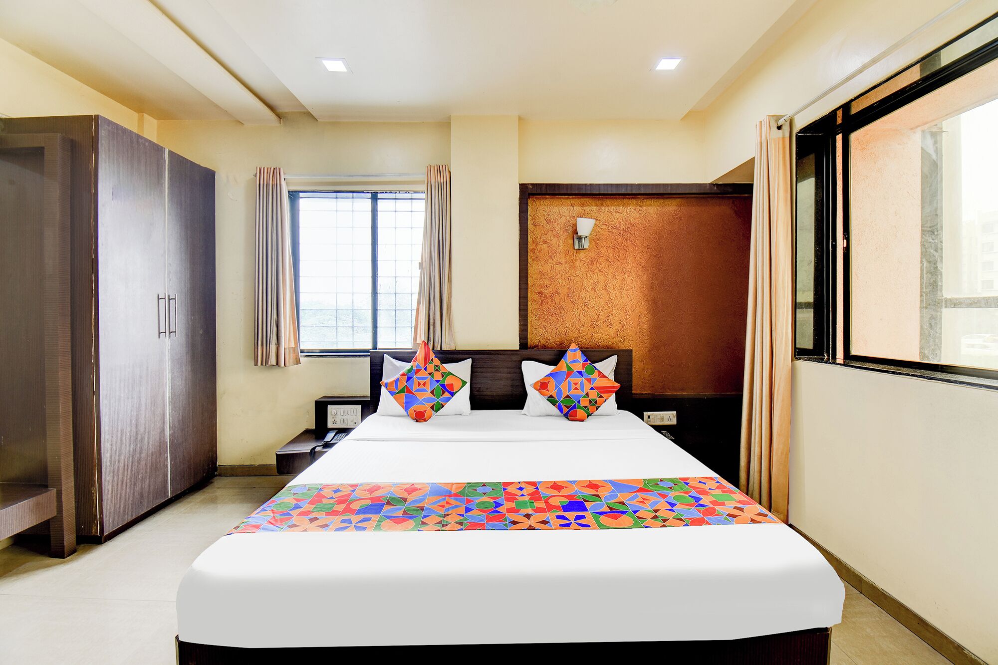 A hotel room with a large bed, a wardrobe, a window with curtains, and a wall-mounted light.