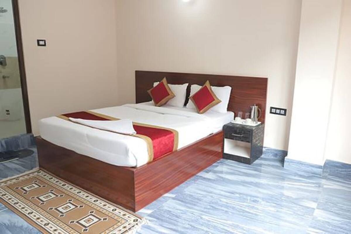 A neatly made bed with a wooden headboard, a bedside table with a lamp, and a patterned rug on a marble floor.