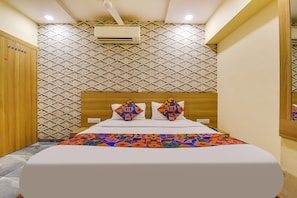 A hotel room with a patterned wallpaper, a wooden headboard, and a colorful bedspread.