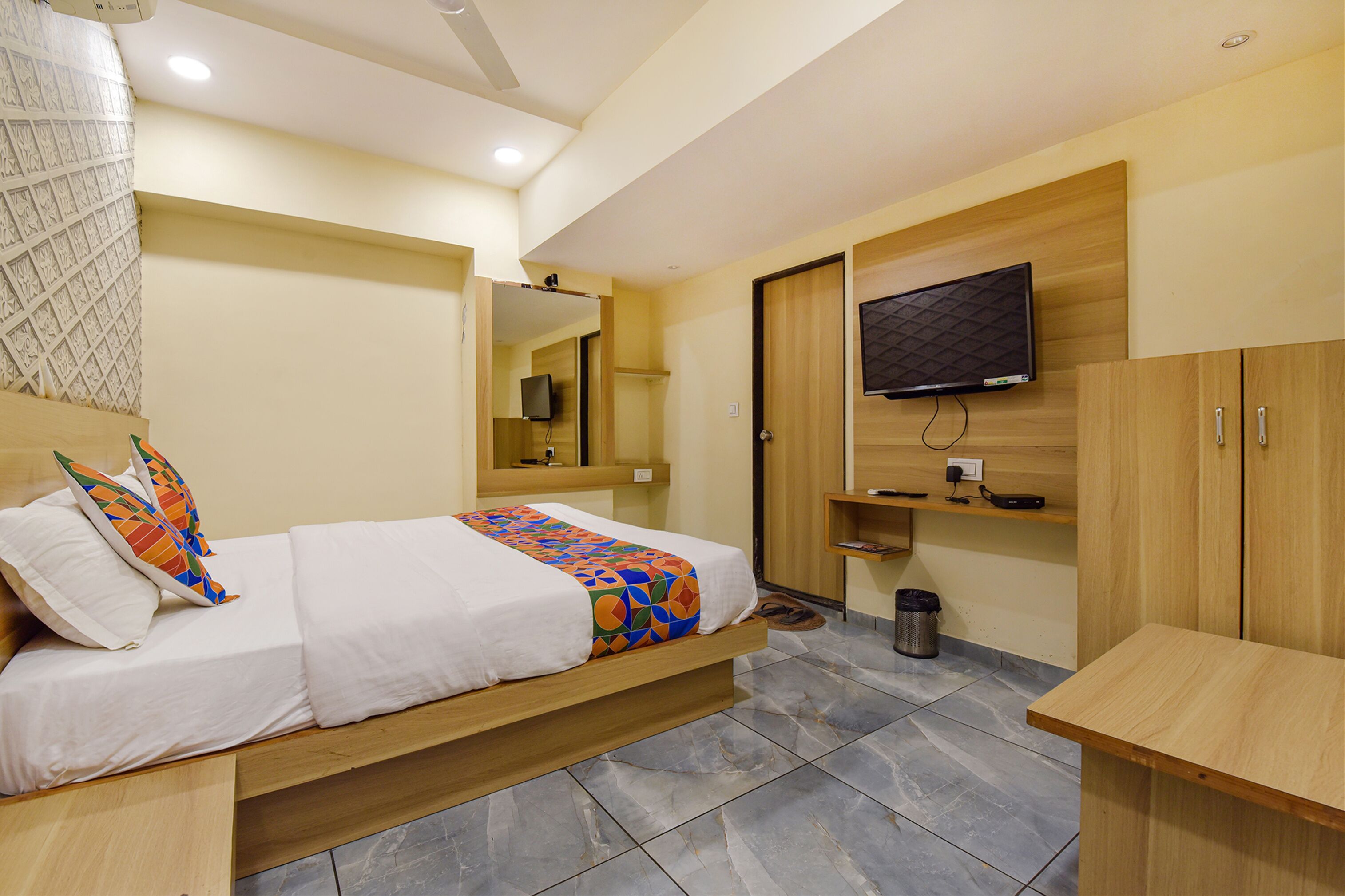 Una habitación de hotel con una cama, un televisor montado en la pared, un armario de madera y una pequeña mesa.