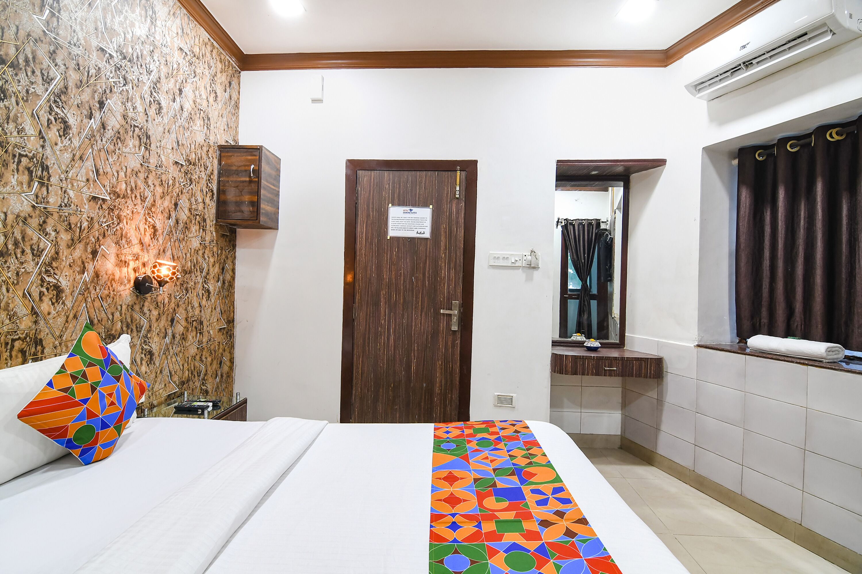 Habitación de hotel con cama, puerta de madera, baño con espejo y toallero.