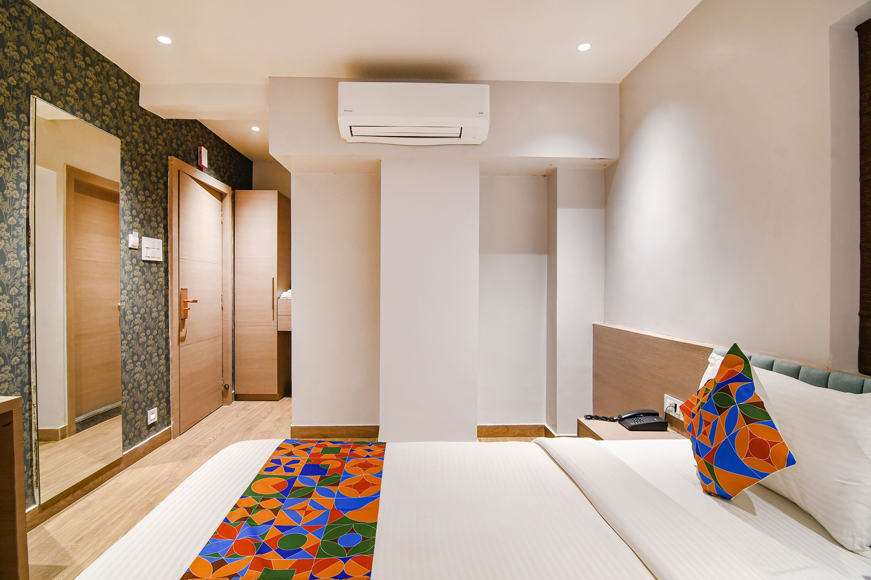 A hotel room with a bed, a nightstand, a phone, and an air conditioning unit.