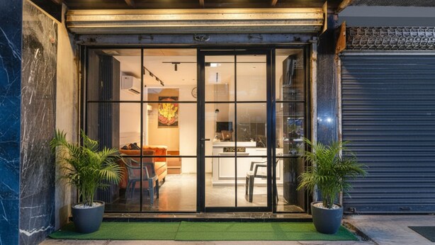 Ingresso di un edificio moderno con una porta in vetro, una reception interna e due piante in vaso all'esterno.