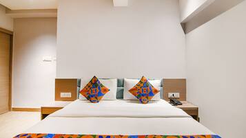 Quarto de hotel moderno com uma cama grande, dois travesseiros com padrões geométricos, uma mesinha de cabeceira com telefone e um cobertor colorido.