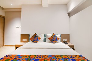 Quarto de hotel moderno com uma cama grande, dois travesseiros com padrões geométricos, uma mesinha de cabeceira com telefone e um cobertor colorido.