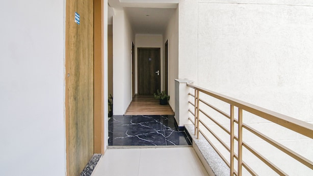 A hallway with a wooden door, a potted plant, and a marble floor. - Fabexpress The Radiant (Gurugram)