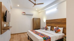A hotel room with a bed, a wardrobe, a television, and a ceiling fan. - Fabexpress The Radiant (Gurugram)