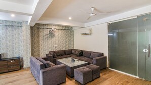 A modern living room with a sectional sofa, ottomans, a glass coffee table, and a ceiling fan. - Fabexpress The Radiant (Gurugram)
