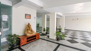 A lobby with a checkered floor, a wooden bench with a statue, and potted plants. - Fabexpress The Radiant (Gurugram)
