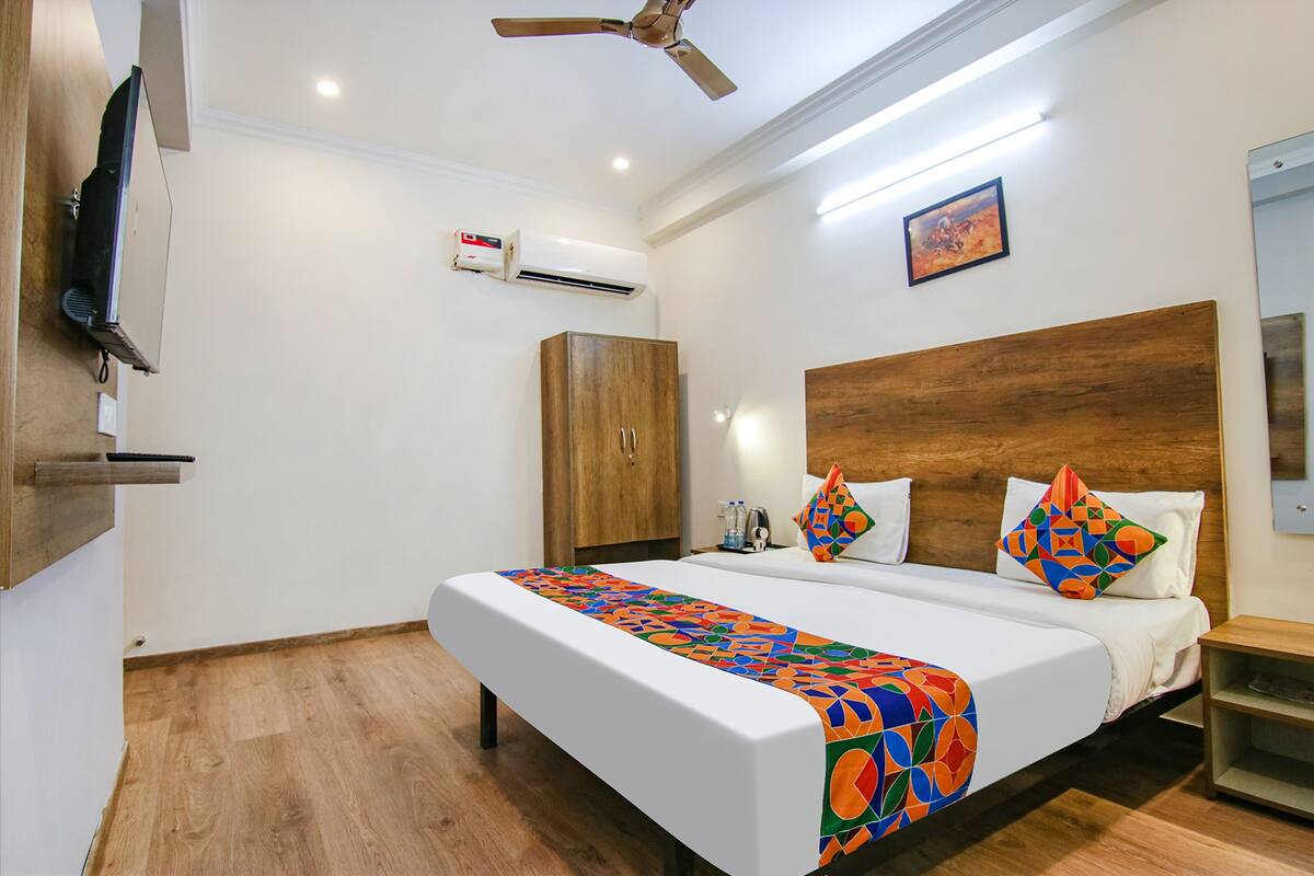 A hotel room with a large bed, a wooden headboard, a ceiling fan, an air conditioning unit, and a television mounted on the wall.