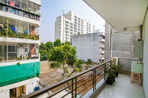 Un balcon doté d’une rambarde en métal, de plantes en pot et offrant une vue sur un immeuble à plusieurs étages en arrière-plan.