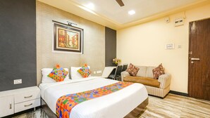 A hotel room with a bed, a sofa, a desk, and a ceiling fan. - Fabexpress Raj Supreme Residency (Chennai)