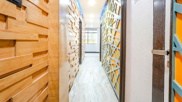 A hallway with wooden paneling on one side and a lattice partition on the other, leading to a room with a door marked "102". - Fabexpress Raj Supreme Residency (Chennai)