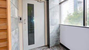 A modern elevator with a glass panel, marble flooring, and a view of the outside through a window. - Fabexpress Raj Supreme Residency (Chennai)