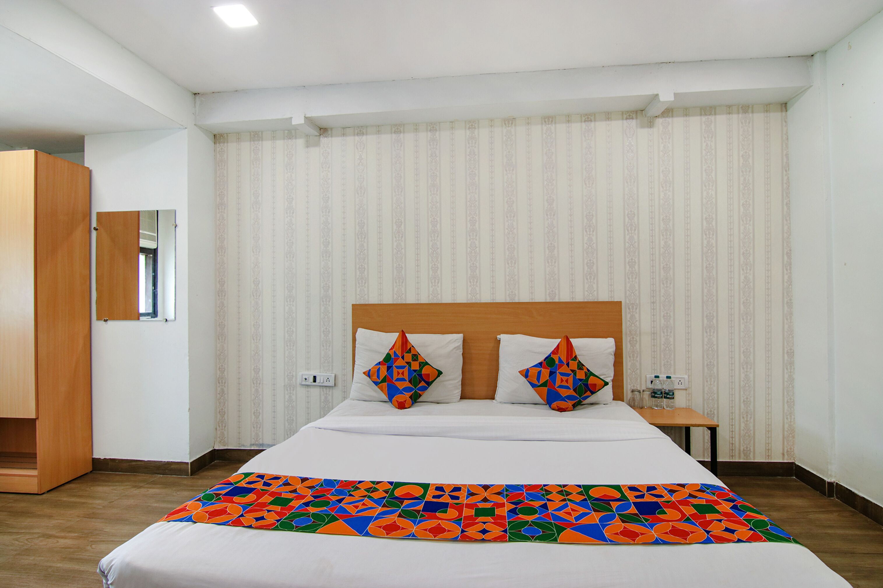 A hotel room with a large bed, a wooden headboard, two nightstands, and a colorful bedspread.