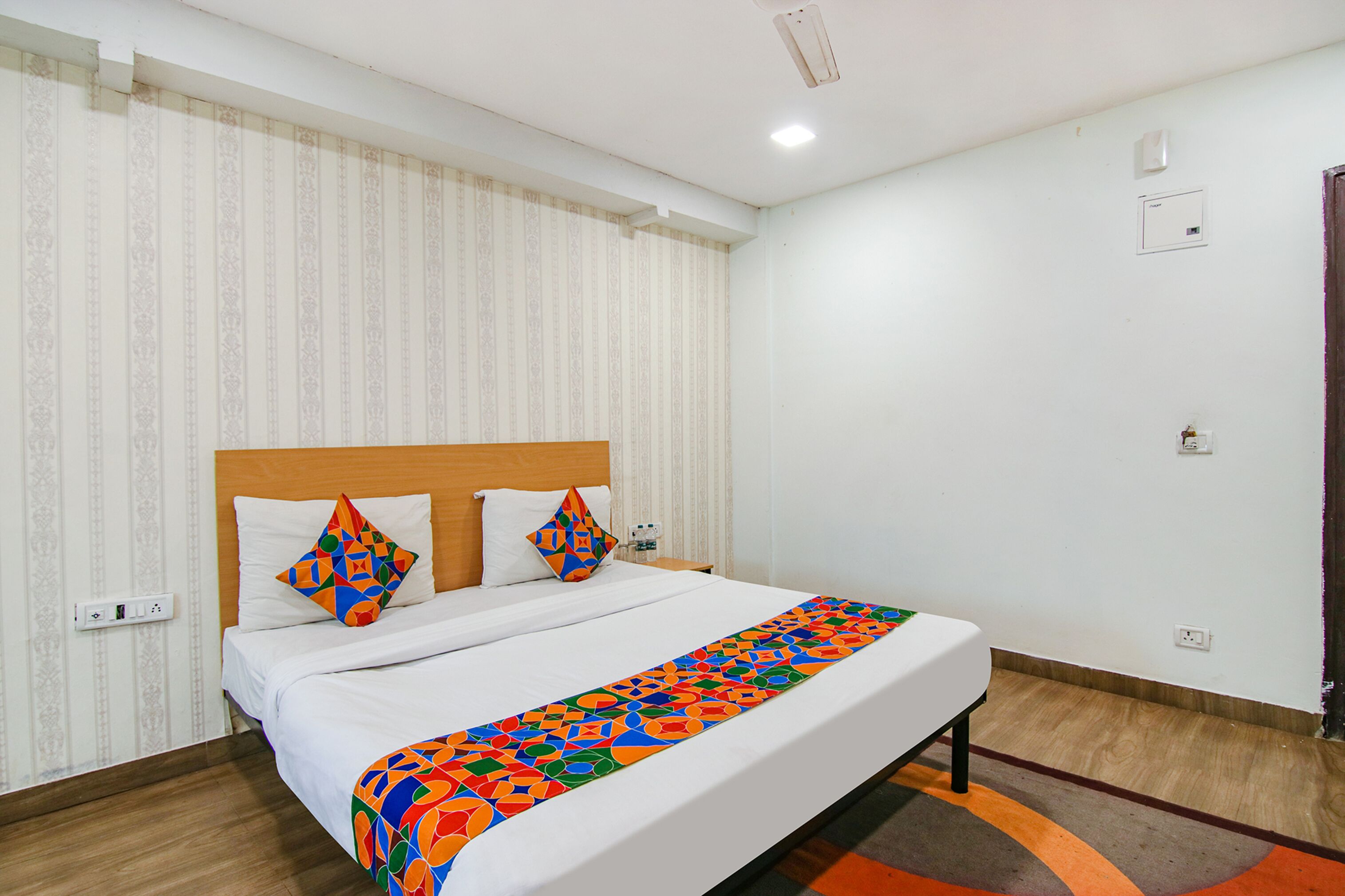 A hotel room with a bed, a headboard, a window with curtains, and a wall-mounted thermostat.