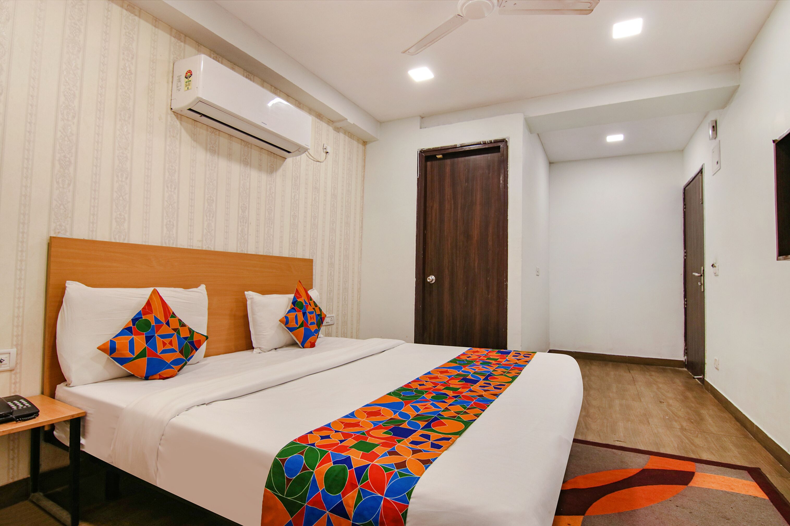 Una camera d'albergo con un letto, una testiera in legno, un condizionatore d'aria, una porta e un pavimento rivestito di moquette.