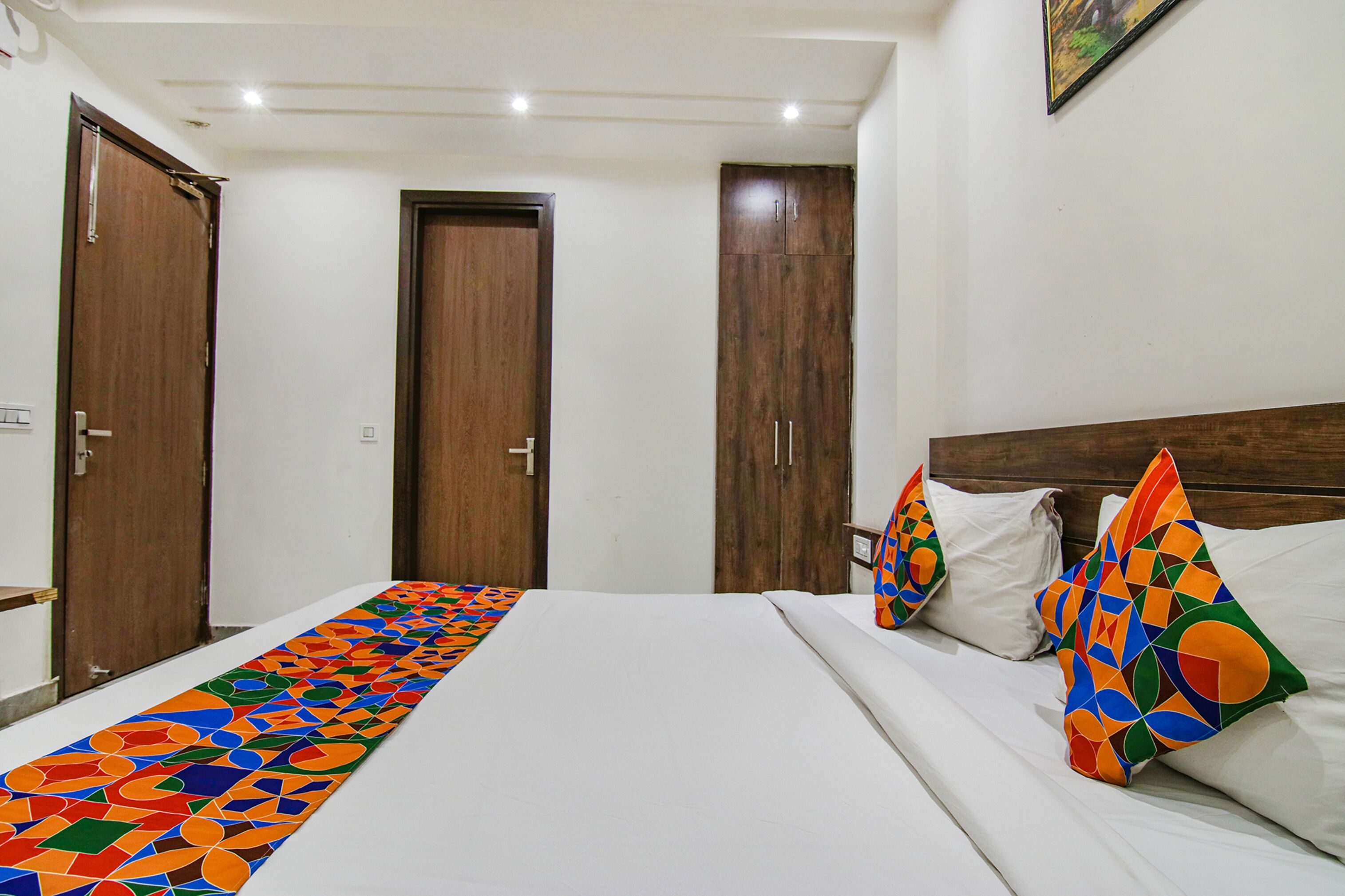 A hotel room with a large bed, two wooden wardrobes, and colorful pillows.