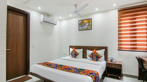 A hotel room with a bed, a desk, a chair, a ceiling fan, an air conditioning unit, a window with blinds, and a painting on the wall. - Fabhotel Moro Rohini Sector 4 (New Delhi)