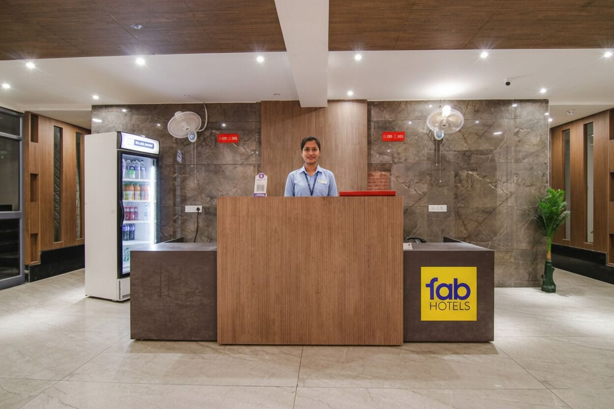 A reception desk with a sign for Fab Hotels, a refrigerator with beverages, and a fan on the wall.