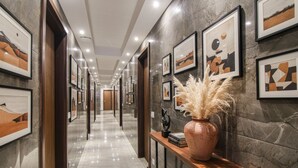 A hallway with framed artwork on the walls, a wooden bench with a vase, and a polished marble floor. - Fabhotel Moro Rohini Sector 4 (New Delhi)