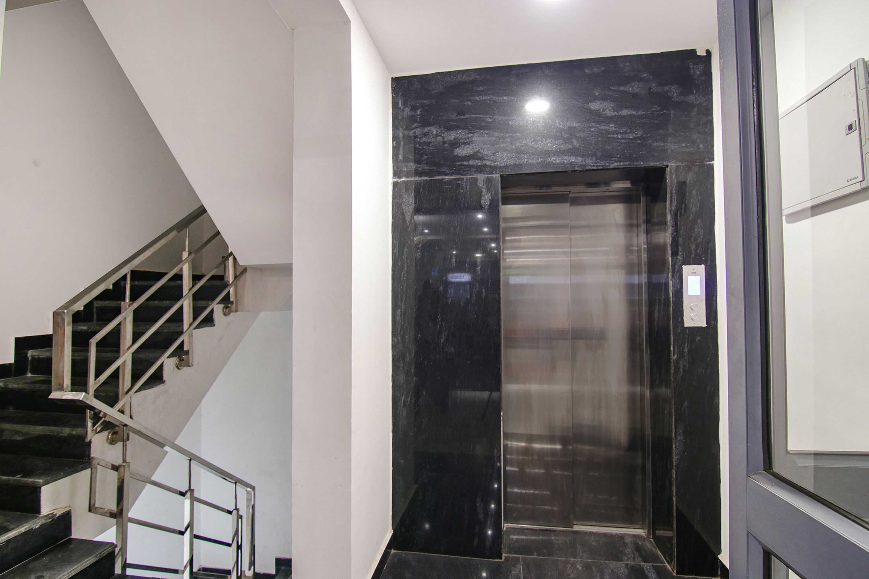 En moderne elevator med sort marmorbeklædning, en trappe med gelændinger i metal og en ensfarvet hvid væg.